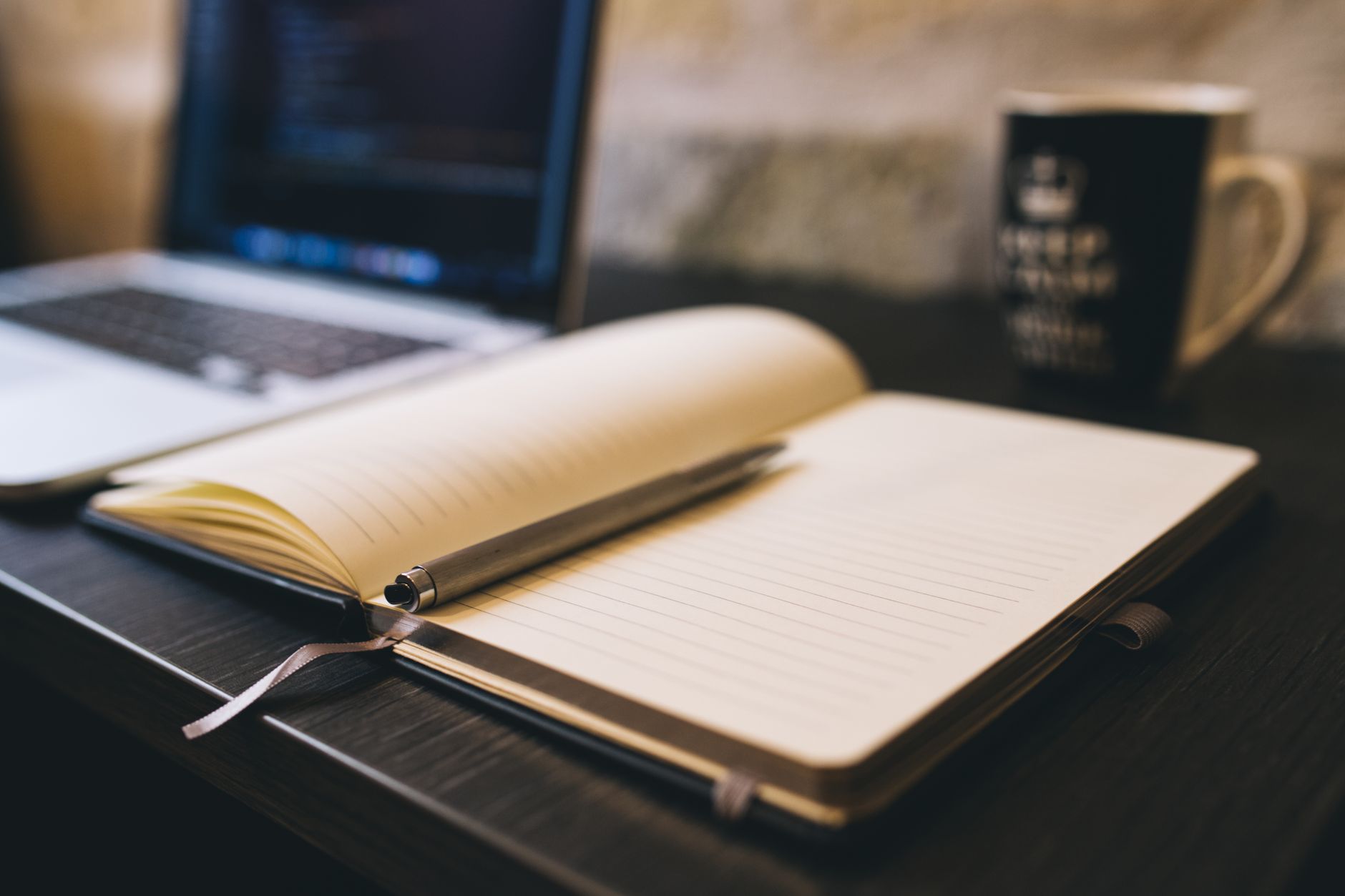 Open notebook and pen on a desk beside a laptop