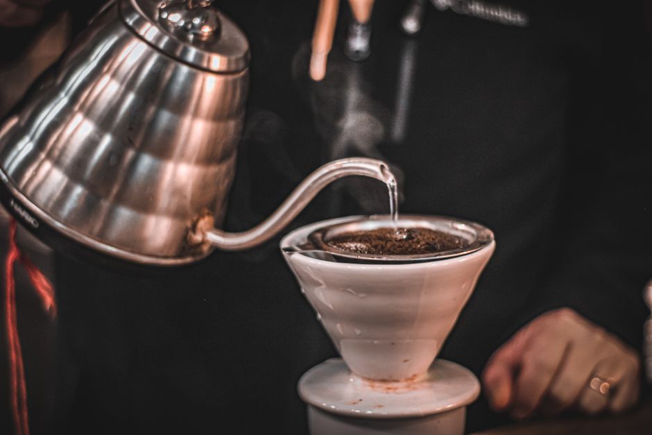 Hot water being poured from a gooseneck kettle over a pour-over coffee maker