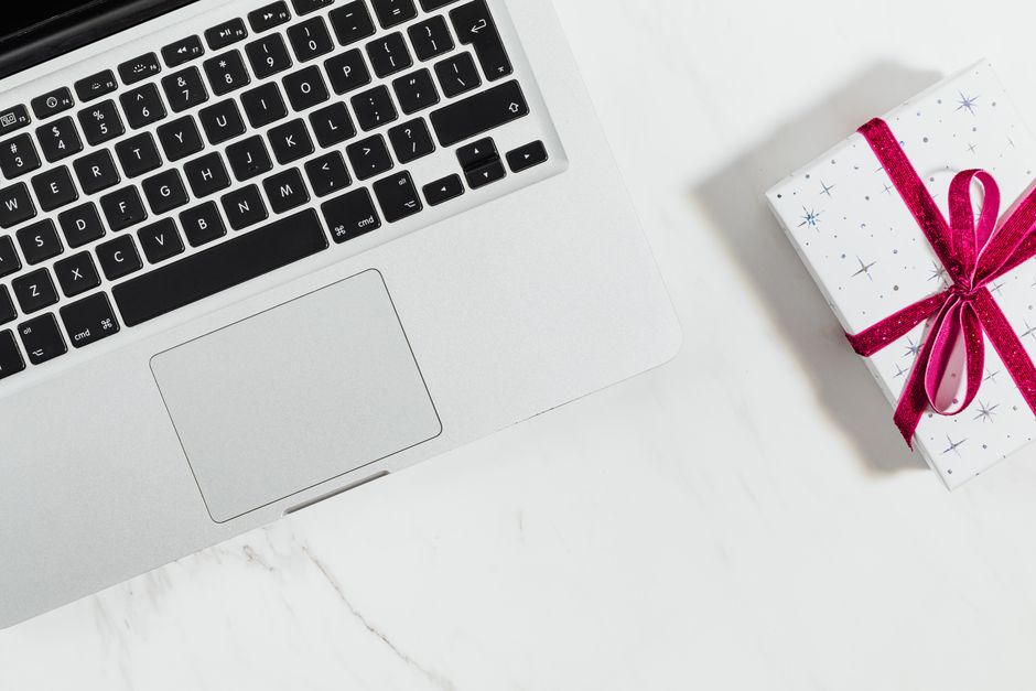 A laptop and a wrapped gift with a red ribbon on a white desk