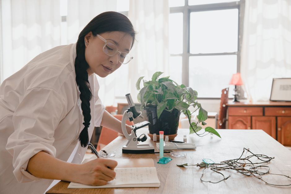 Researcher writing notes while working with a microscope