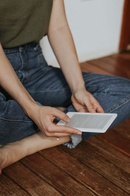 A person sitting cross-legged reading a paper on a small e-ink e-reader