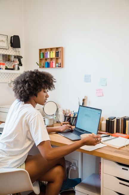 A graduate student working at a laptop on a home study desk with supplies