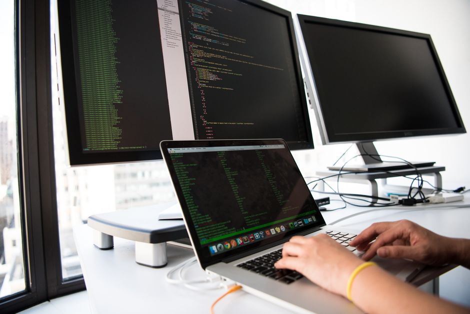 Developer writing code on a laptop with multiple monitors